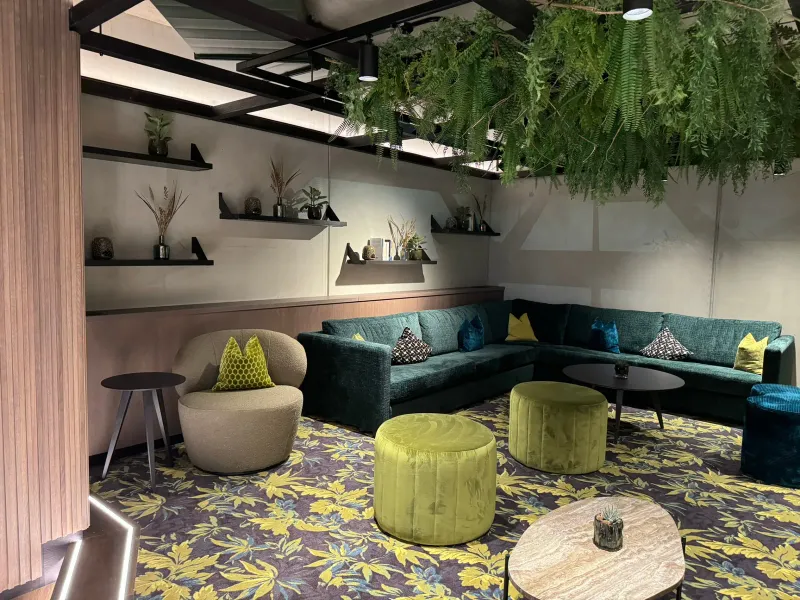 Mitarbeiterlounge mit grünem Ecksofa, Hängepflanzen und Blümenteppich