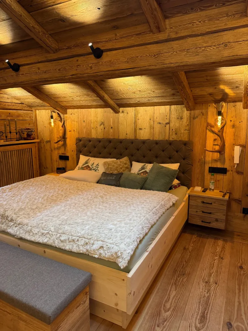 Schlafzimmer mit Zirbenholzbett und Geweihlampen