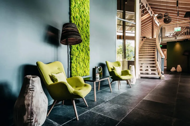 Lobby mit Mooswand, Holztreppe und grünen Sesseln
